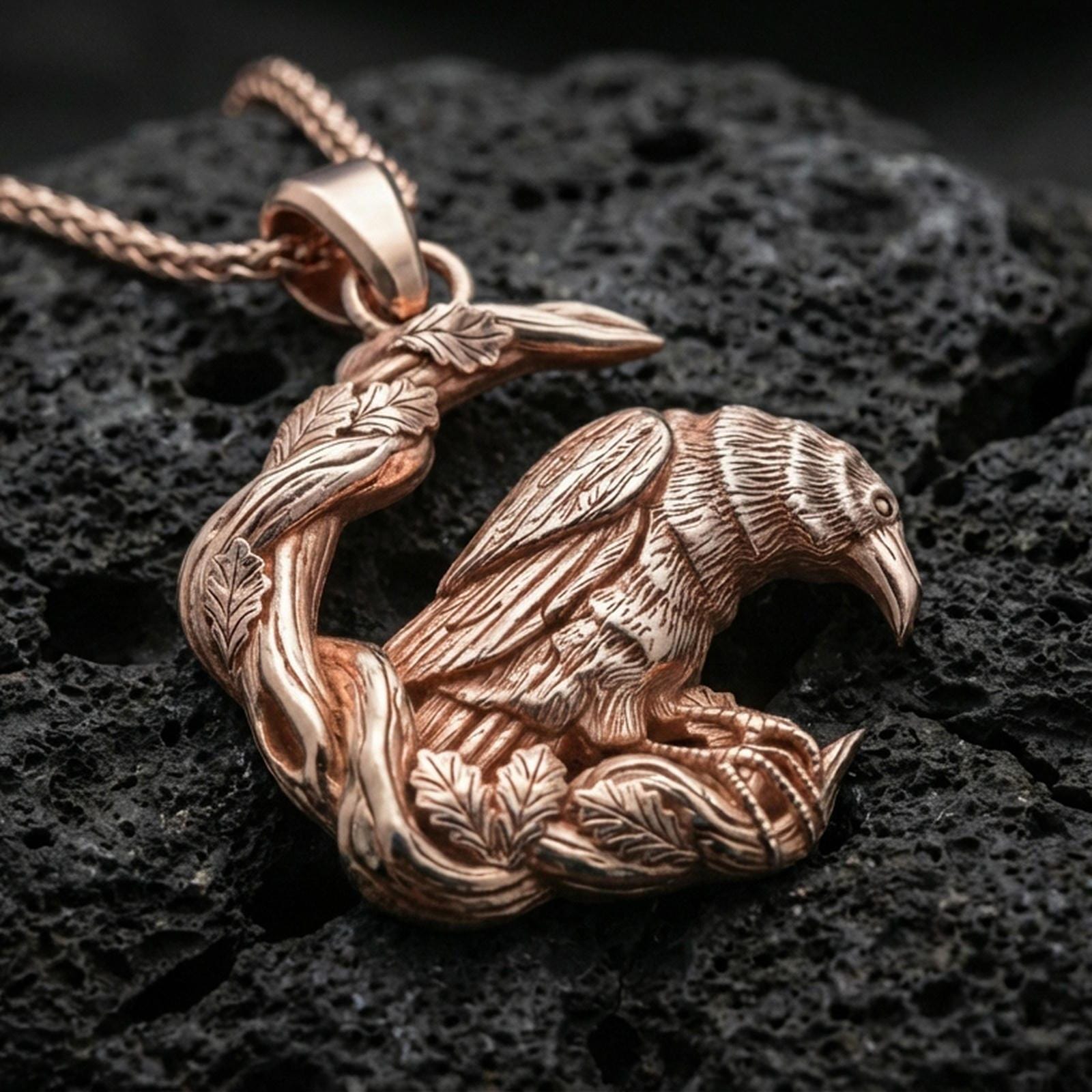 Rose gold plated Viking raven pendant necklace presented on dark volcanic rock in a premium close-up jewelry photograph.