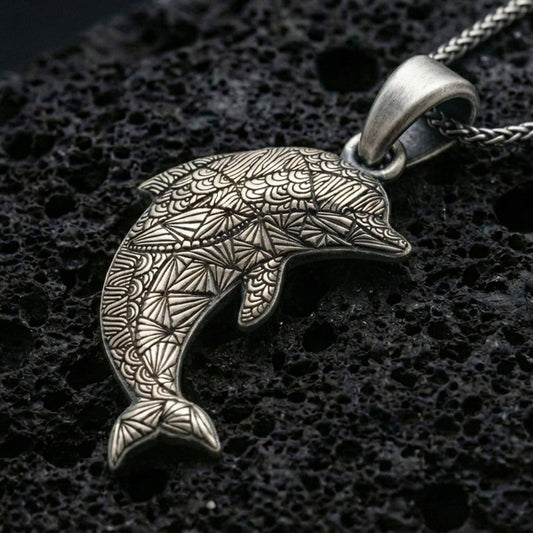 Sterling silver dolphin pendant necklace with an oxidized finish resting on textured volcanic rock, captured in a close-up premium studio composition.