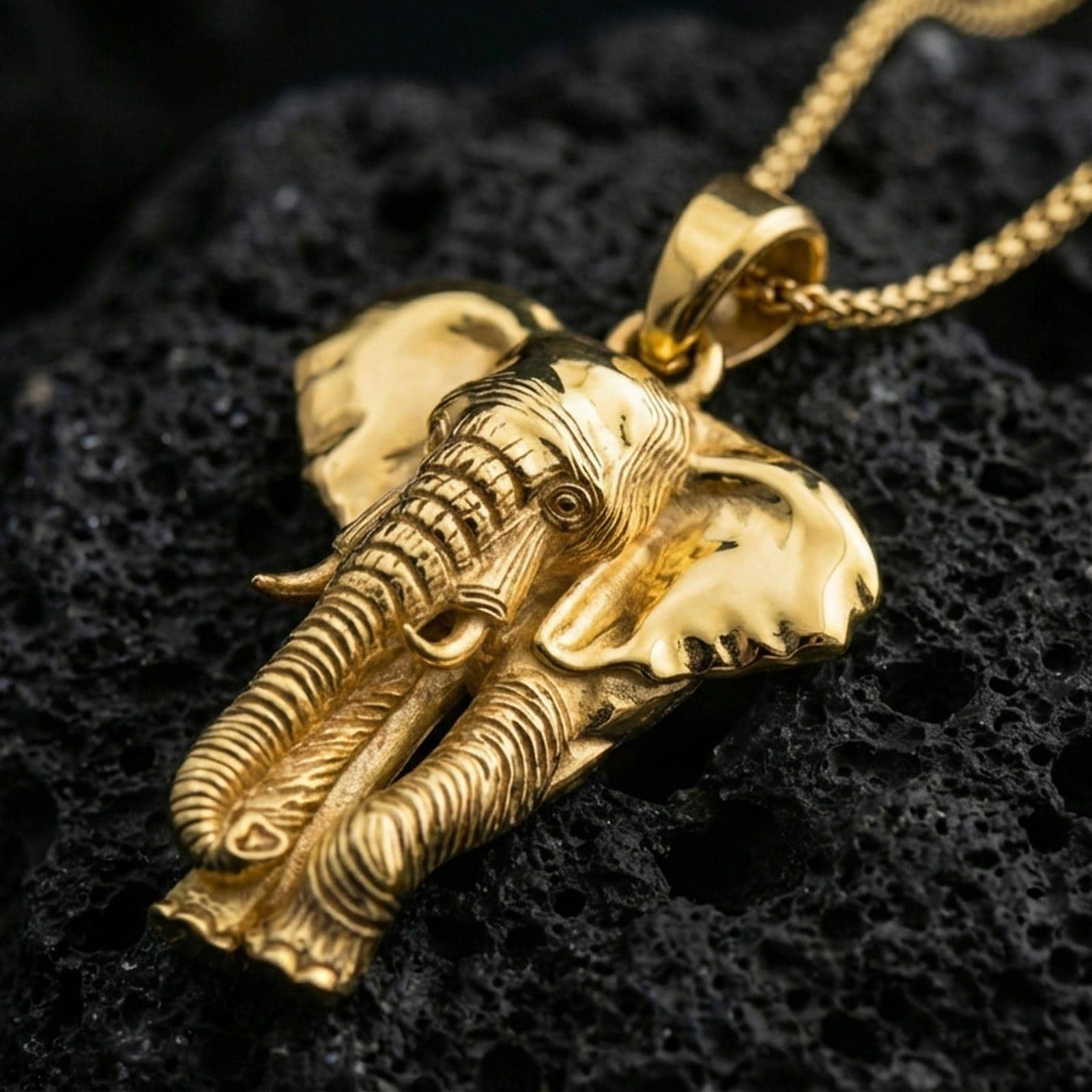 Gold plated elephant pendant necklace presented on porous volcanic rock, highlighting the dimensional animal design in a luxurious close-up jewelry image.