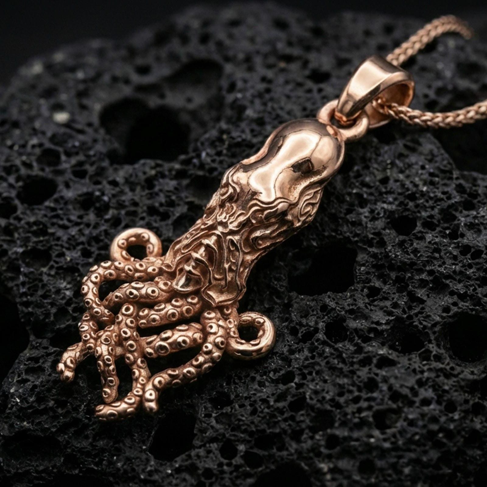 Rose gold plated octopus pendant necklace on dark volcanic rock, photographed in a detailed premium studio macro view.