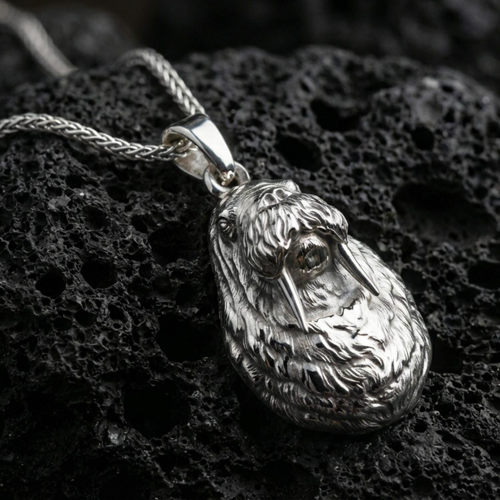 Polished silver walrus pendant necklace displayed on black volcanic rock, shown in a refined macro product shot with detailed tusk and fur texture.