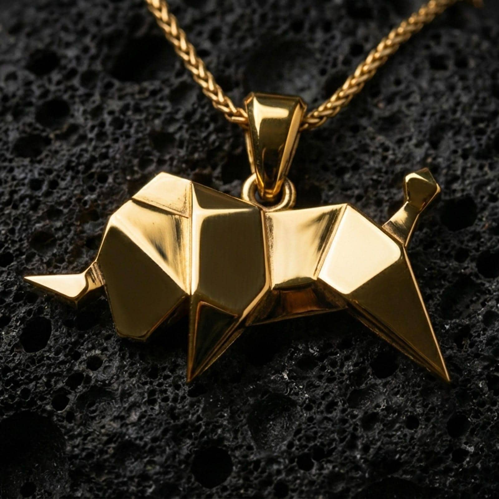 Gold plated origami elephant pendant necklace presented on porous volcanic rock, highlighting the angular animal silhouette in a luxurious close-up jewelry image.