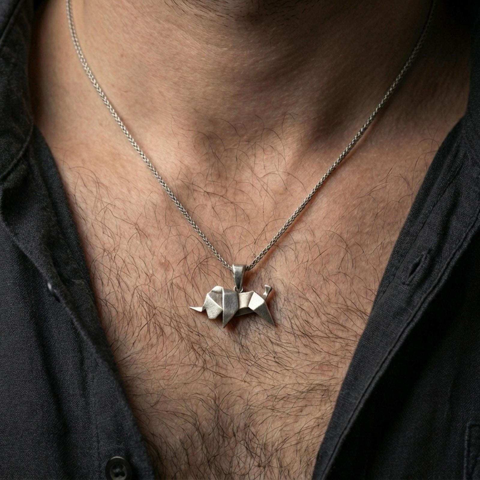 Oxidized origami elephant pendant necklace worn on the neck, styled in a dark lifestyle portrait with an open shirt and masculine presentation.