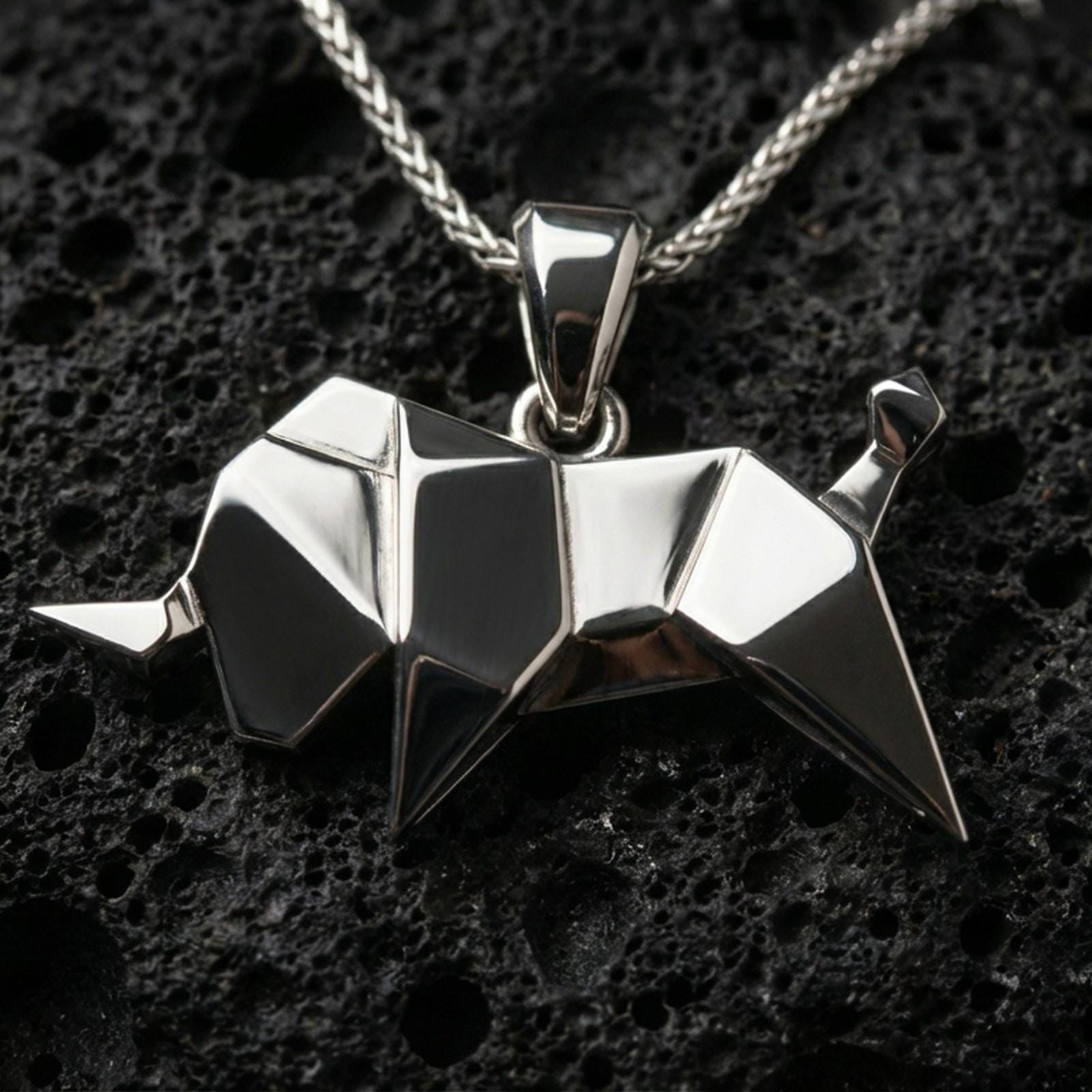 Polished silver origami elephant pendant necklace displayed on black volcanic rock, shown in a refined macro product shot with sharp geometric folds.
