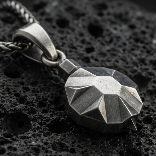 Sterling silver origami tortoise pendant necklace with an oxidized finish resting on textured volcanic rock, captured in a close-up premium studio composition.