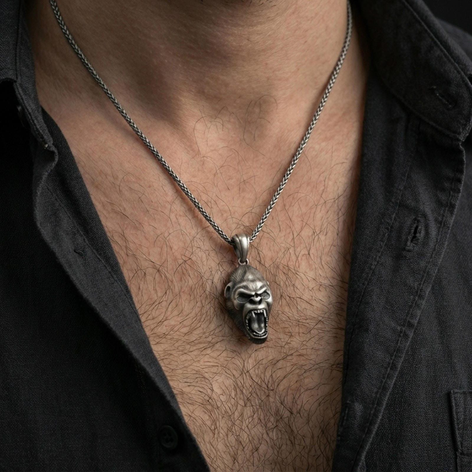 Oxidized gorilla head pendant necklace worn on the neck, styled in a dark lifestyle portrait with an open shirt and masculine presentation.