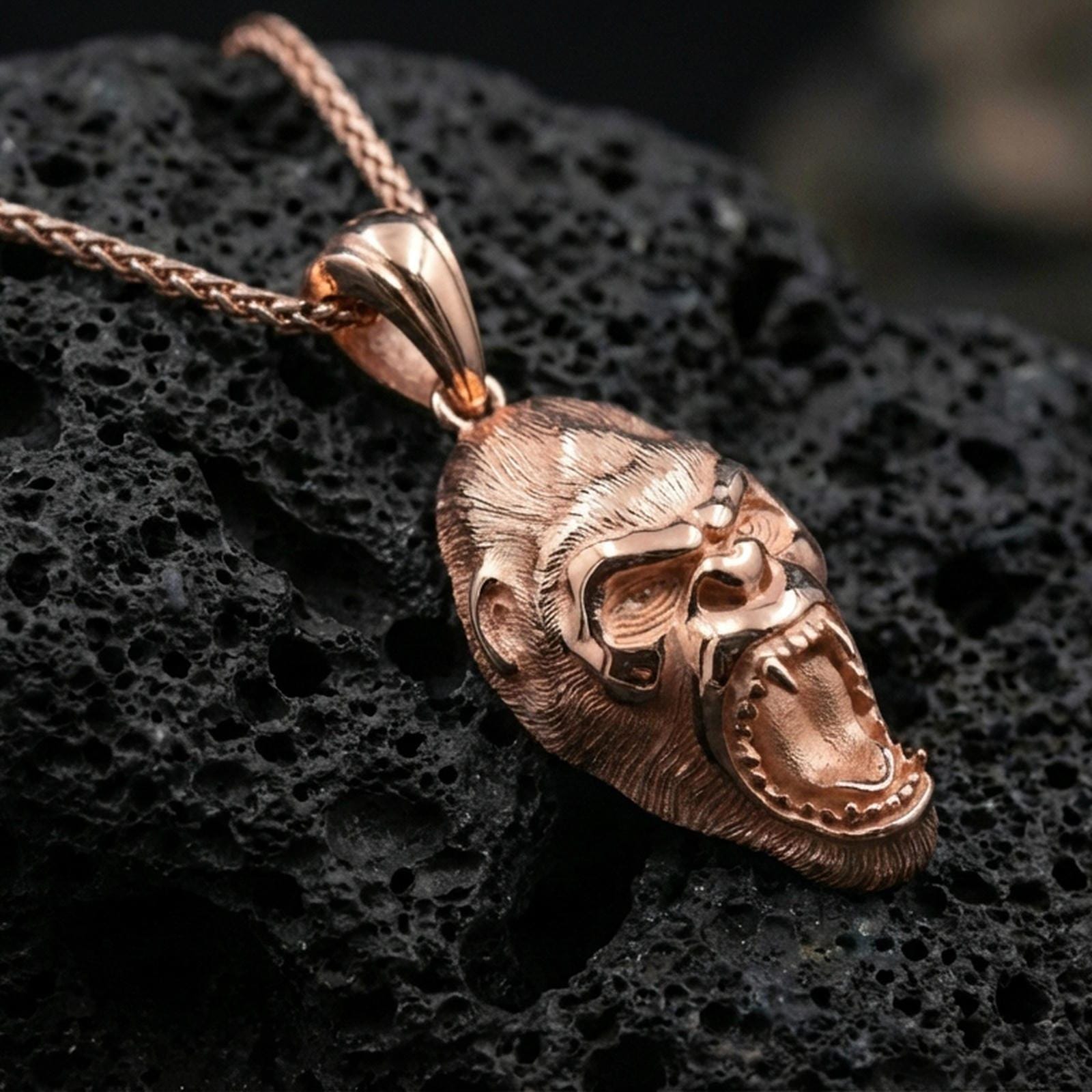 Rose gold plated gorilla head pendant necklace on dark volcanic rock, photographed in a detailed premium studio macro view.
