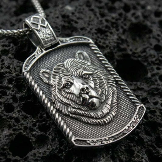 Sterling silver bear pendant necklace with an oxidized finish resting on textured volcanic rock, captured in a close-up premium studio composition.