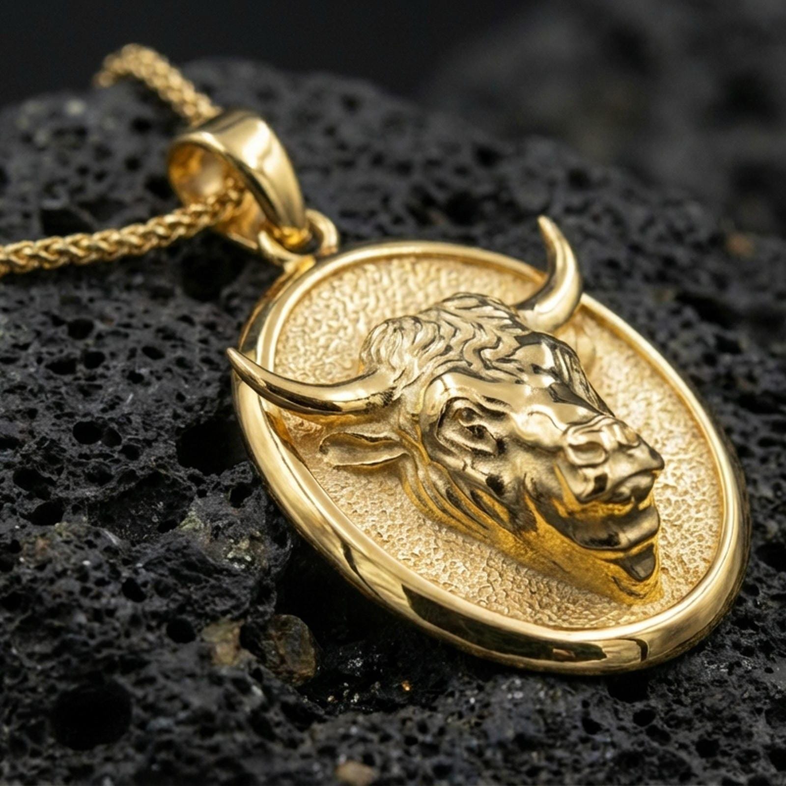 Gold plated bull pendant necklace presented on porous volcanic rock, highlighting the raised animal relief in a luxurious close-up jewelry image.
