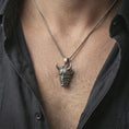 Load image into Gallery viewer, Oxidized Oni mask pendant necklace worn on the neck, styled in a dark lifestyle portrait with an open shirt and masculine presentation.
