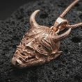 Load image into Gallery viewer, Rose gold plated Oni mask pendant necklace on dark volcanic rock, photographed in a detailed premium studio macro view.
