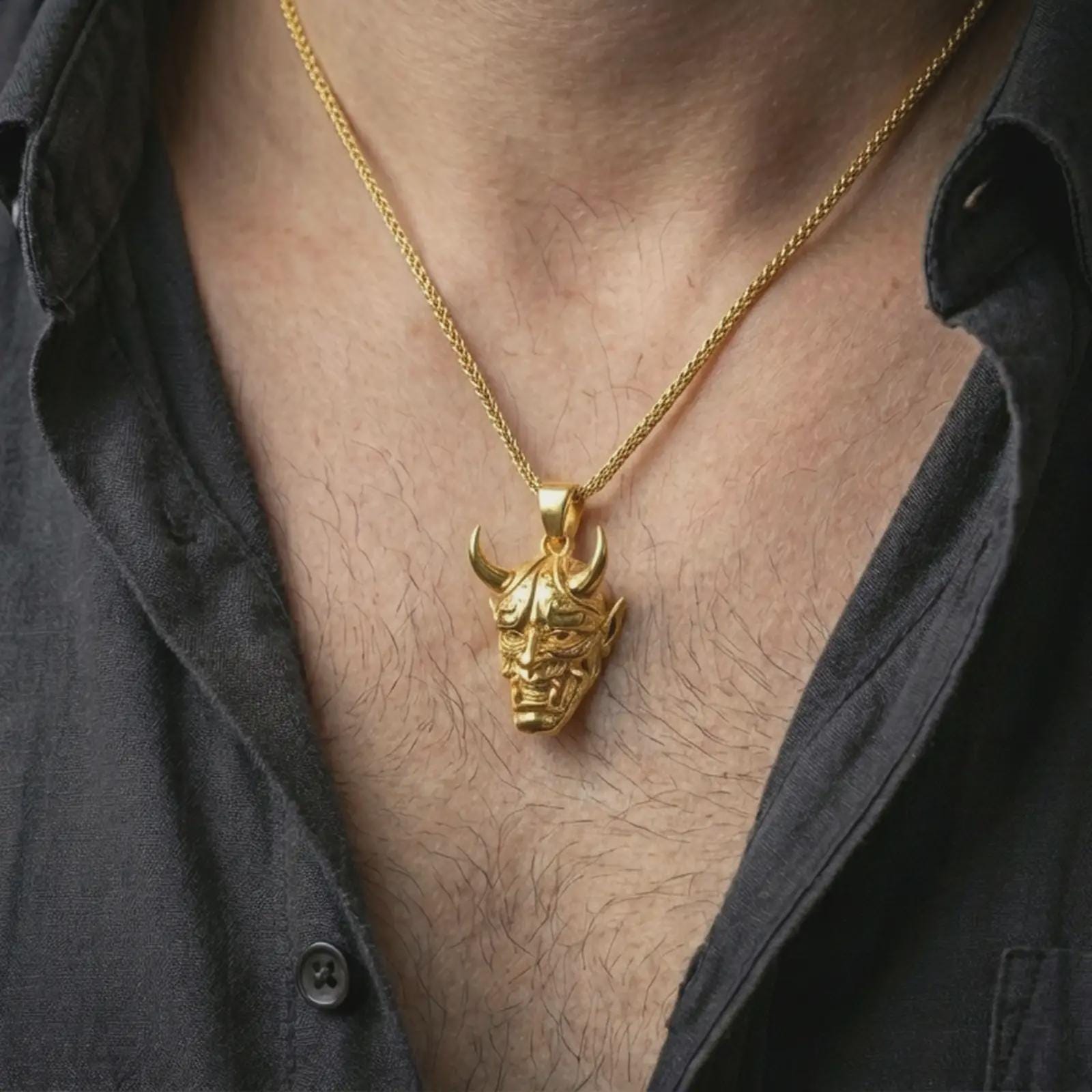 Gold plated Oni mask pendant necklace worn on the neck, captured on a human model in a premium dark-toned lifestyle frame.