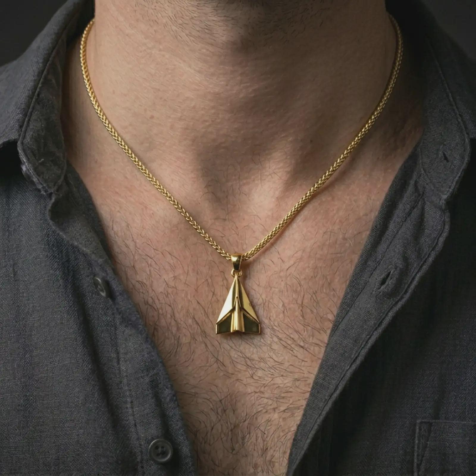Gold plated origami airplane pendant necklace worn on the neck, captured on a human model in a premium dark-toned lifestyle frame.