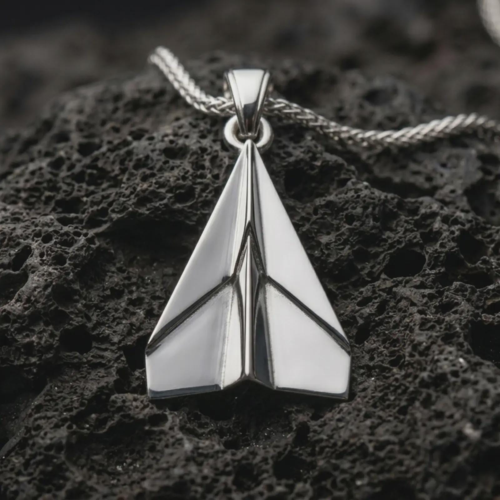 Polished silver origami airplane pendant necklace displayed on black volcanic rock, shown in a refined macro product shot with clean geometric folds and sharp aviation-inspired lines.