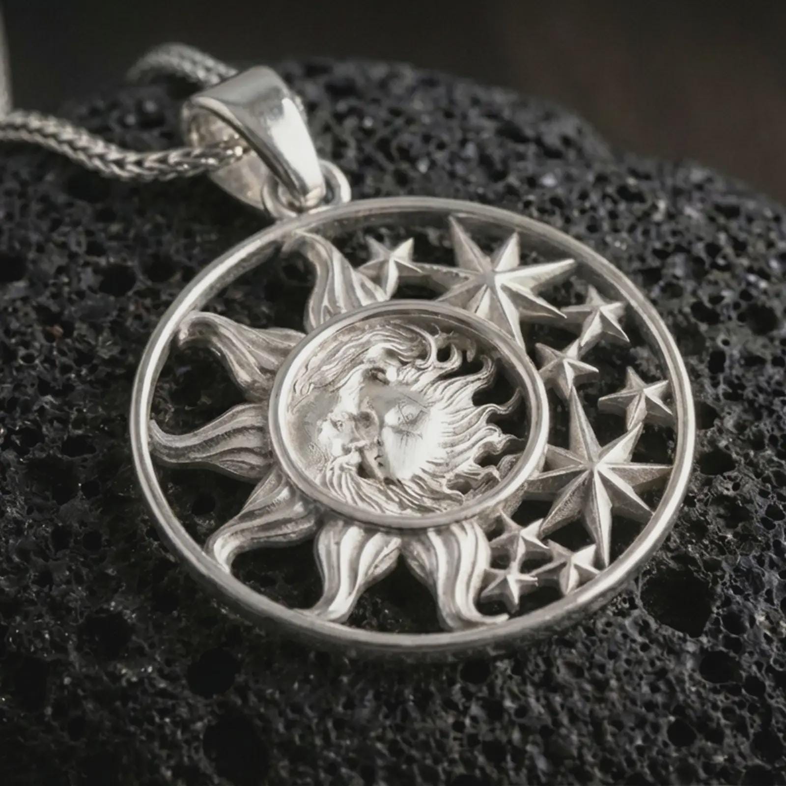 Polished silver sun and moon pendant necklace displayed on black volcanic rock, shown in a refined macro product shot with celestial face detail and star relief.