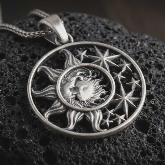 Sterling silver sun and moon pendant necklace with an oxidized finish resting on textured volcanic rock, captured in a close-up premium studio composition.
