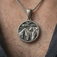 Load image into Gallery viewer, Oxidized mountain landscape pendant necklace worn on the neck, styled in a dark lifestyle portrait with an open shirt and masculine presentation.
