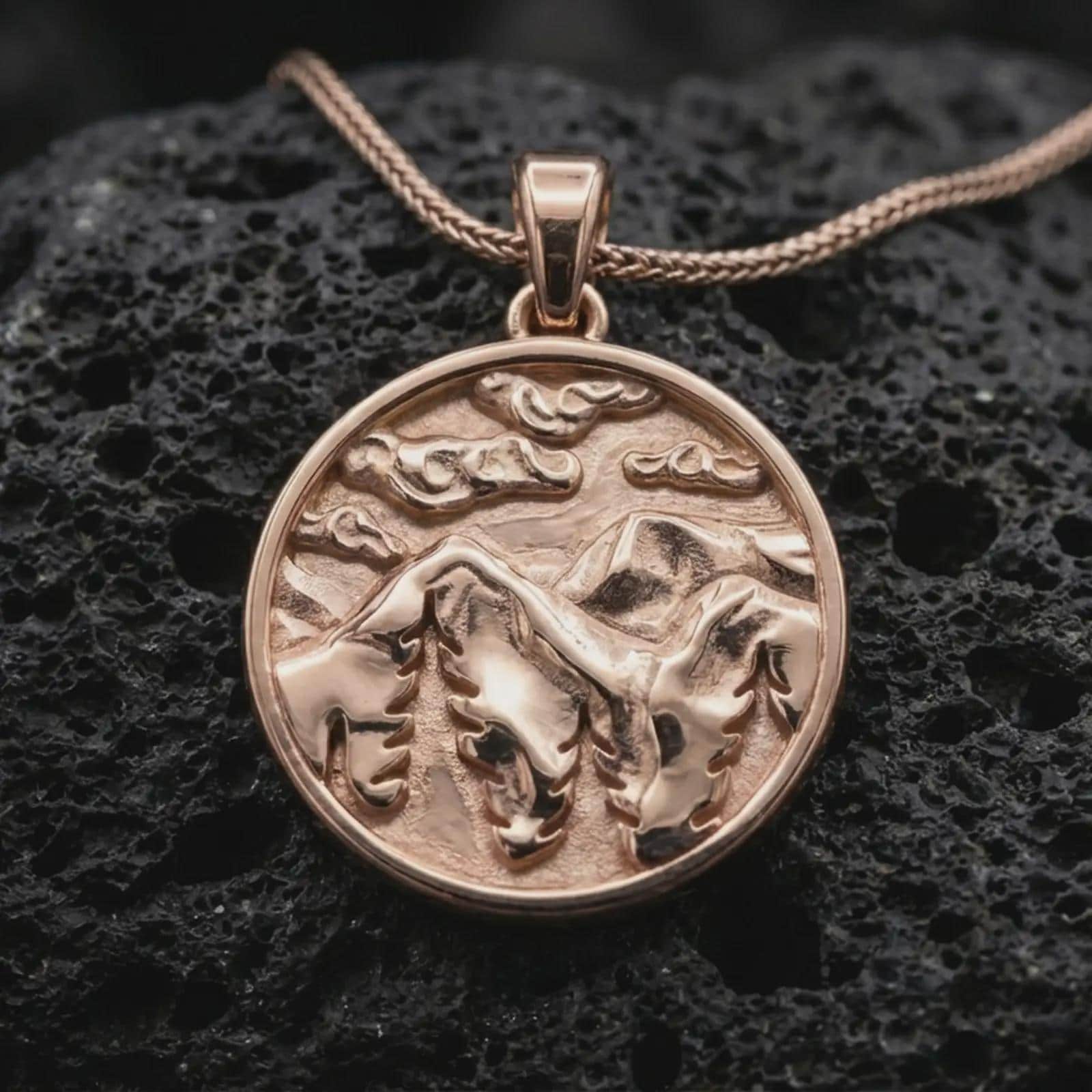 Rose gold plated mountain landscape pendant necklace on dark volcanic rock, photographed in a detailed premium studio macro view.