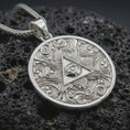 Load image into Gallery viewer, Polished silver Eye of Providence pendant necklace displayed on black volcanic rock, shown in a refined macro product shot with triangular eye symbol and flowing ornamental relief.

