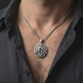 Load image into Gallery viewer, Oxidized Masonic emblem pendant necklace worn on the neck, styled in a dark lifestyle portrait with an open shirt and masculine presentation.
