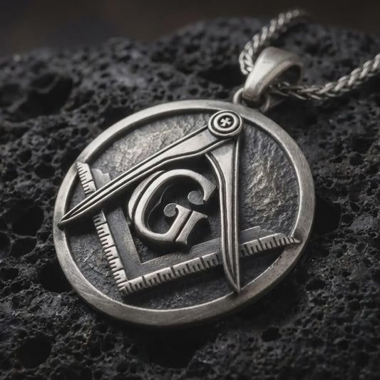Sterling silver Masonic emblem pendant necklace with an oxidized finish resting on textured volcanic rock, captured in a close-up premium studio composition.