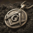 Load image into Gallery viewer, Bronze Masonic emblem pendant necklace with an oxidized finish resting on textured volcanic rock, captured in a close-up premium studio composition.
