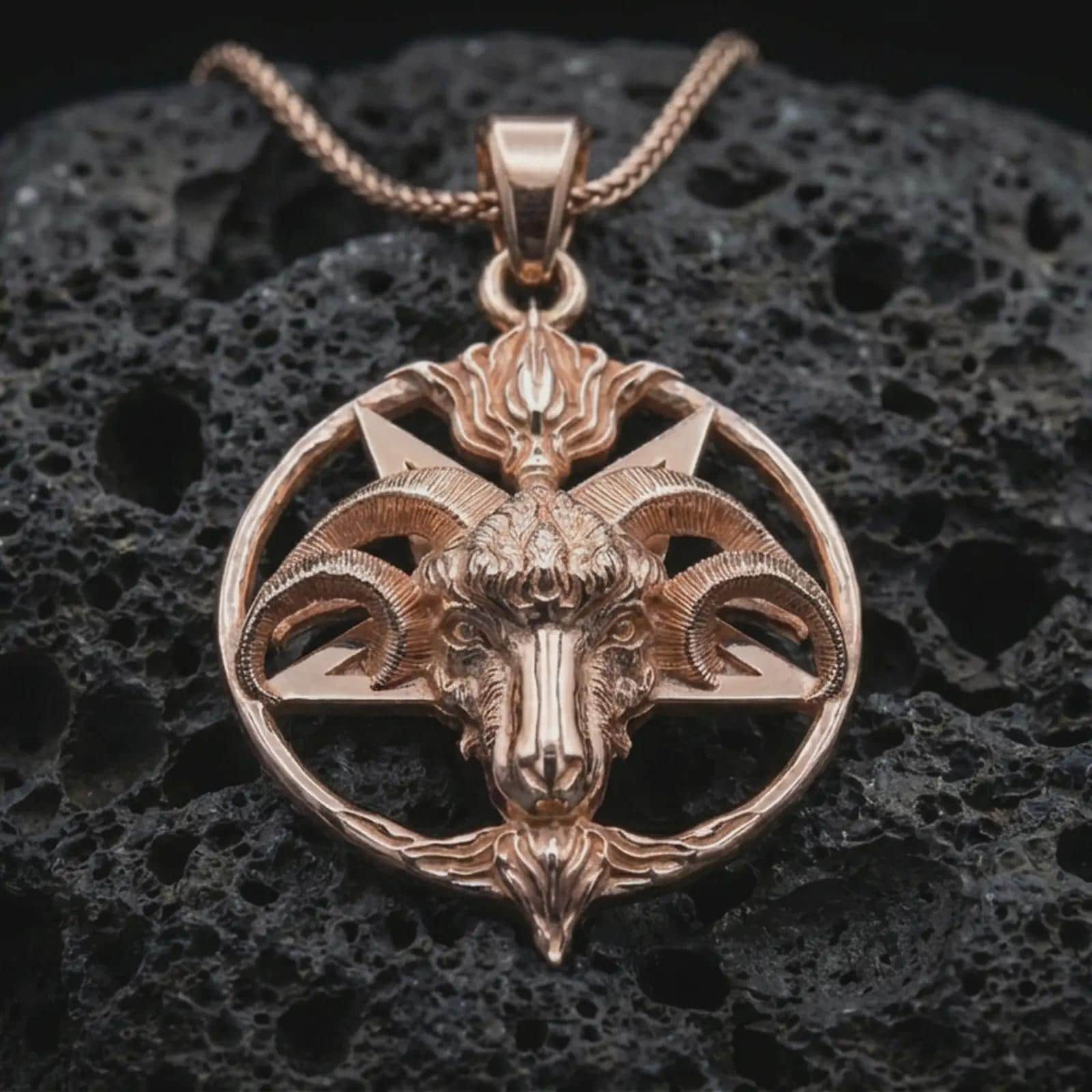 Rose gold plated Baphomet goat head pendant necklace on dark volcanic rock, photographed in a detailed premium studio macro view.