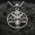 Load image into Gallery viewer, Polished silver Baphomet goat head pendant necklace displayed on black volcanic rock, shown in a refined macro product shot with pentagram frame, ram horns, and occult-inspired relief.
