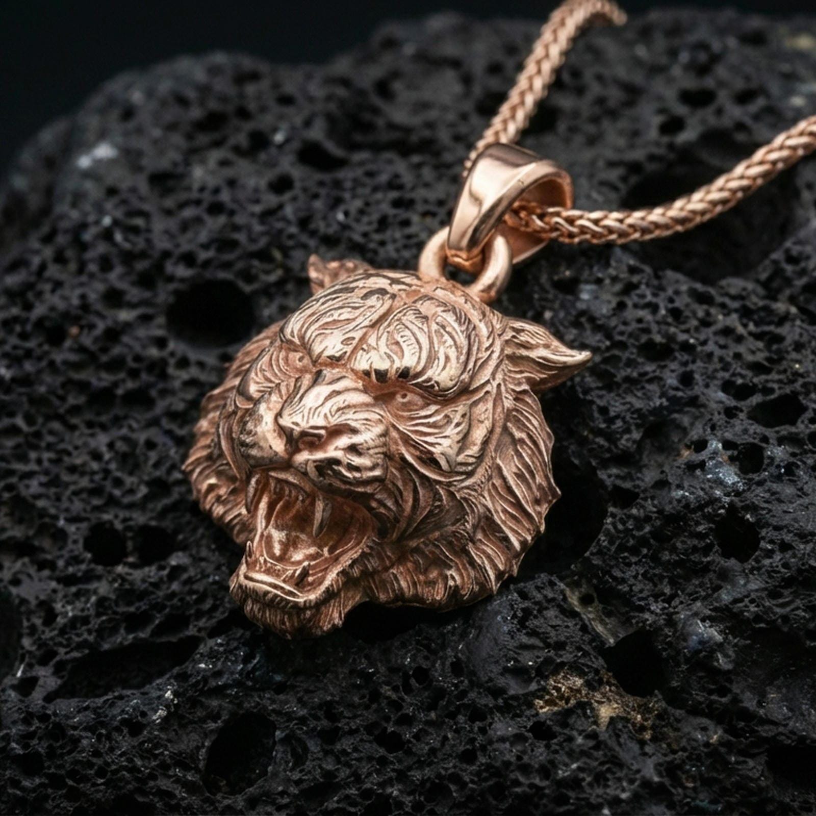 Rose gold plated tiger lion pendant necklace on dark volcanic rock, photographed in a detailed premium studio macro view.