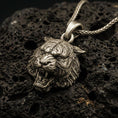 Load image into Gallery viewer, Bronze tiger lion pendant necklace with an oxidized finish resting on textured volcanic rock, captured in a close-up premium studio composition.
