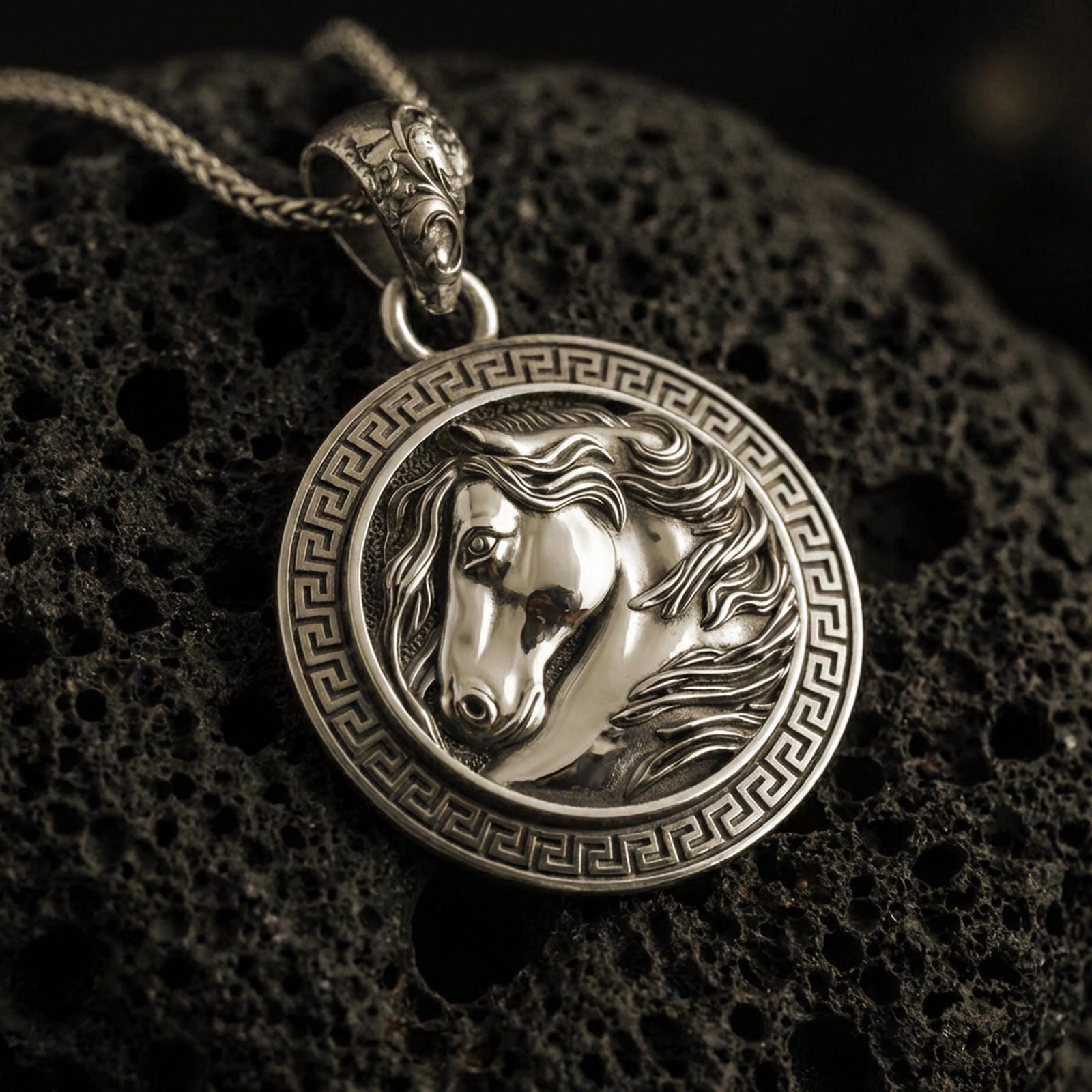 Bronze horse head pendant necklace with an oxidized finish resting on textured volcanic rock, captured in a close-up premium studio composition.