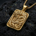 Load image into Gallery viewer, Gold plated cobra pendant necklace presented on porous volcanic rock, highlighting the rectangular medallion form and sculpted snake motif in a luxurious close-up jewelry image.
