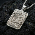 Load image into Gallery viewer, Polished silver cobra pendant necklace displayed on black volcanic rock, shown in a refined macro product shot with detailed serpent and foliage relief.
