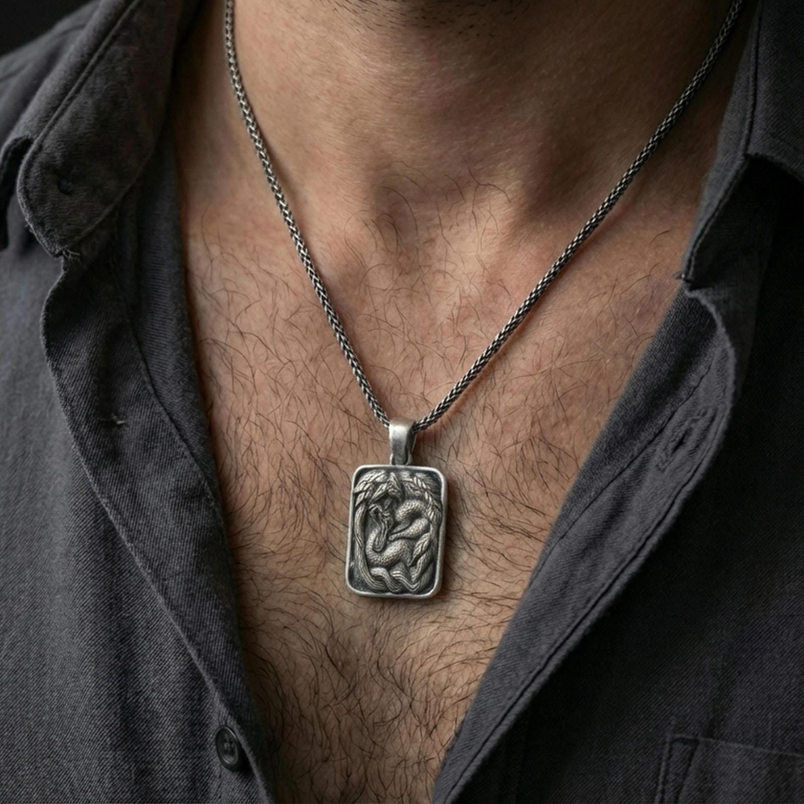 Oxidized cobra pendant necklace worn on the neck, styled in a dark lifestyle portrait with an open shirt and masculine presentation.