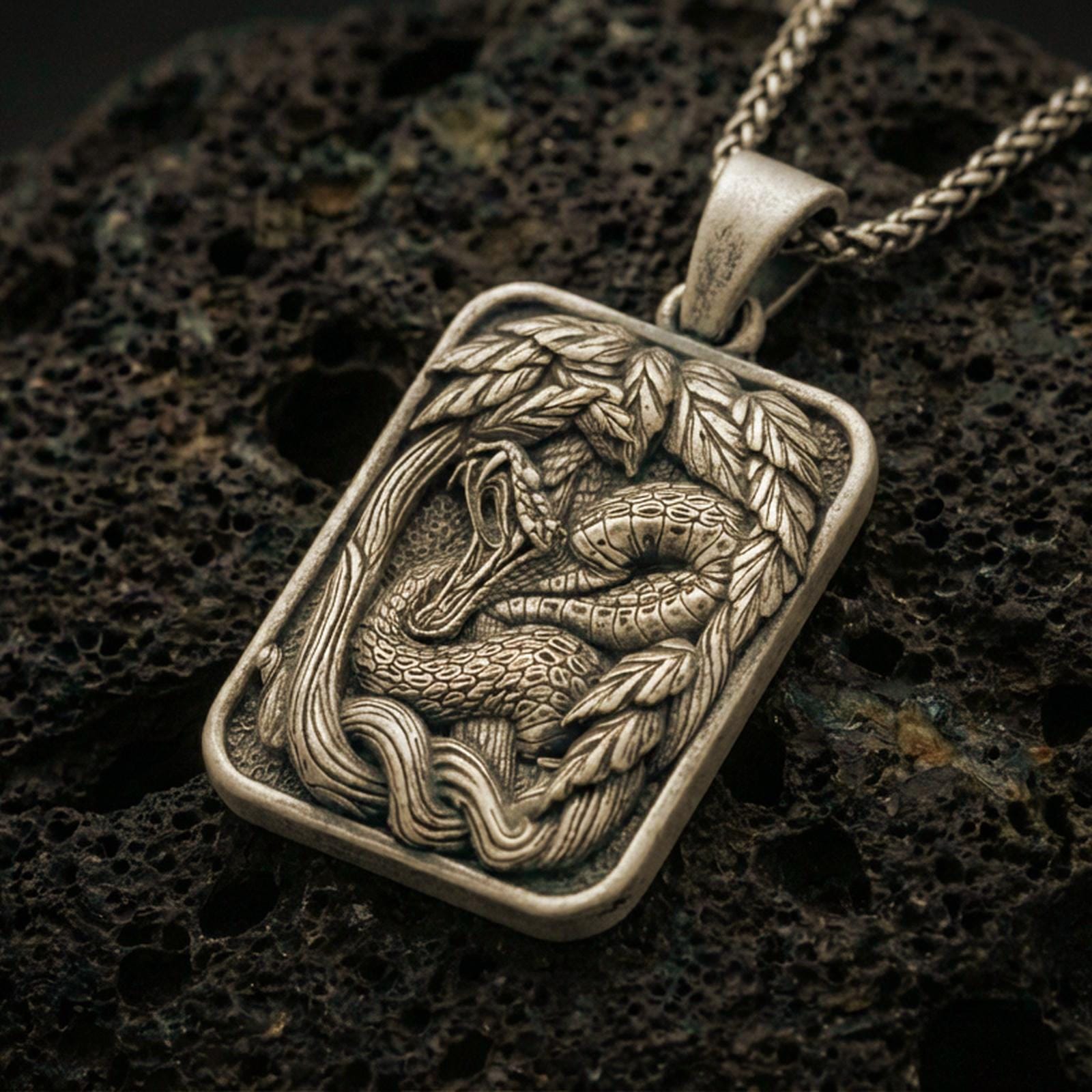 Bronze cobra pendant necklace with an oxidized finish resting on textured volcanic rock, captured in a close-up premium studio composition.
