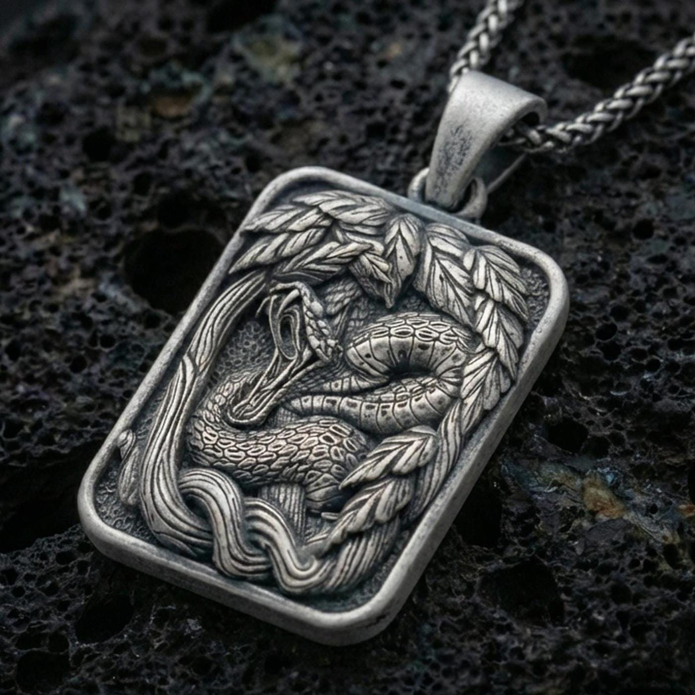 Sterling silver cobra pendant necklace with an oxidized finish resting on textured volcanic rock, captured in a close-up premium studio composition.