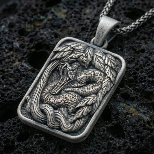 Sterling silver cobra pendant necklace with an oxidized finish resting on textured volcanic rock, captured in a close-up premium studio composition.