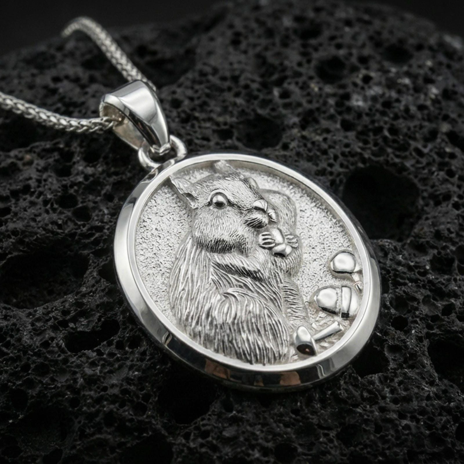 Polished silver squirrel pendant necklace displayed on black volcanic rock, shown in a refined macro product shot with detailed fur and acorn relief.