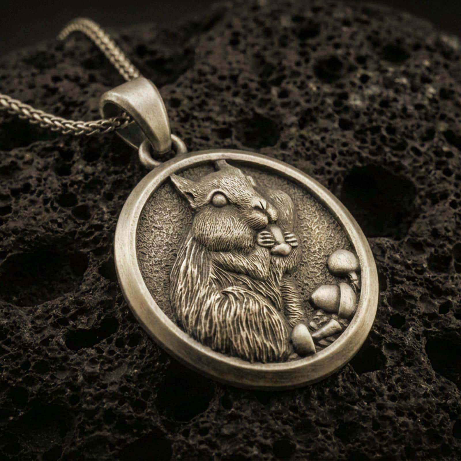 Bronze squirrel pendant necklace with an oxidized finish resting on textured volcanic rock, captured in a close-up premium studio composition.