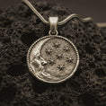 Load image into Gallery viewer, Bronze moon and stars pendant necklace with an oxidized finish resting on textured volcanic rock, captured in a close-up premium studio composition.
