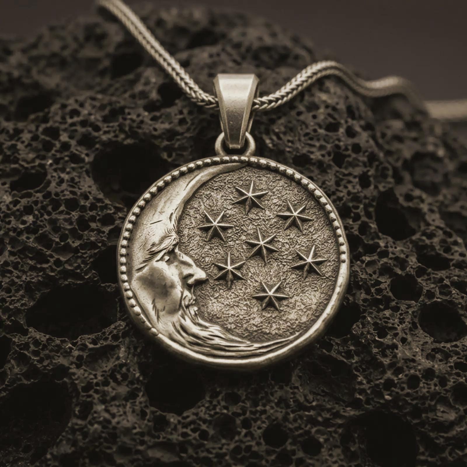 Bronze moon and stars pendant necklace with an oxidized finish resting on textured volcanic rock, captured in a close-up premium studio composition.
