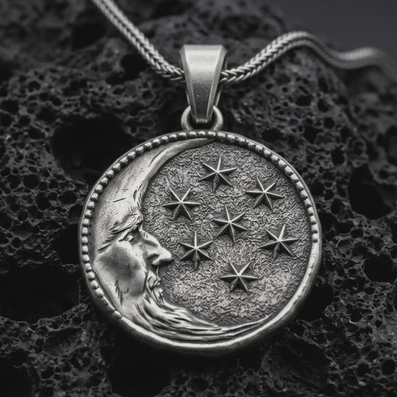 Sterling silver moon and stars pendant necklace with an oxidized finish resting on textured volcanic rock, captured in a close-up premium studio composition.