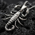 Load image into Gallery viewer, Sterling silver scorpion pendant necklace with an oxidized finish resting on textured volcanic rock, captured in a close-up premium studio composition.
