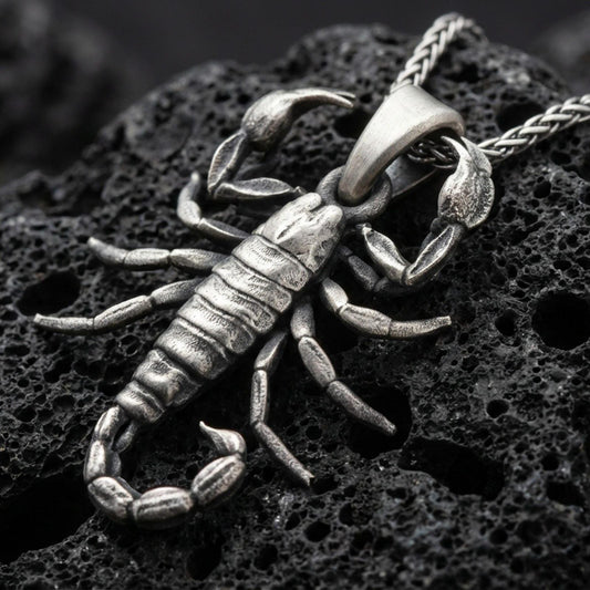 Sterling silver scorpion pendant necklace with an oxidized finish resting on textured volcanic rock, captured in a close-up premium studio composition.