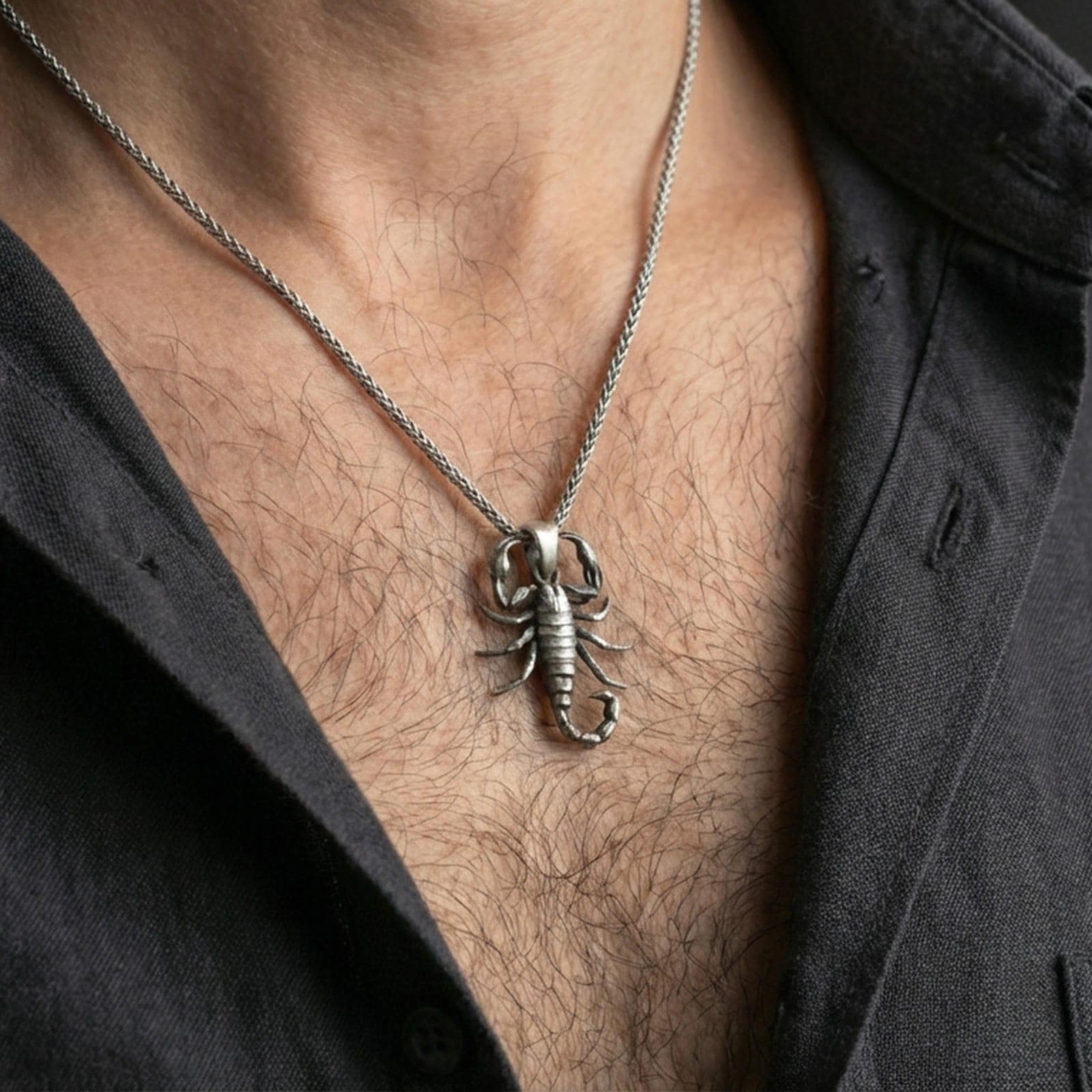 Oxidized scorpion pendant necklace worn on the neck, styled in a dark lifestyle portrait with an open shirt and masculine presentation.