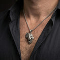 Load image into Gallery viewer, Oxidized lion head pendant necklace worn on the neck, styled in a dark lifestyle portrait with an open shirt and masculine presentation.
