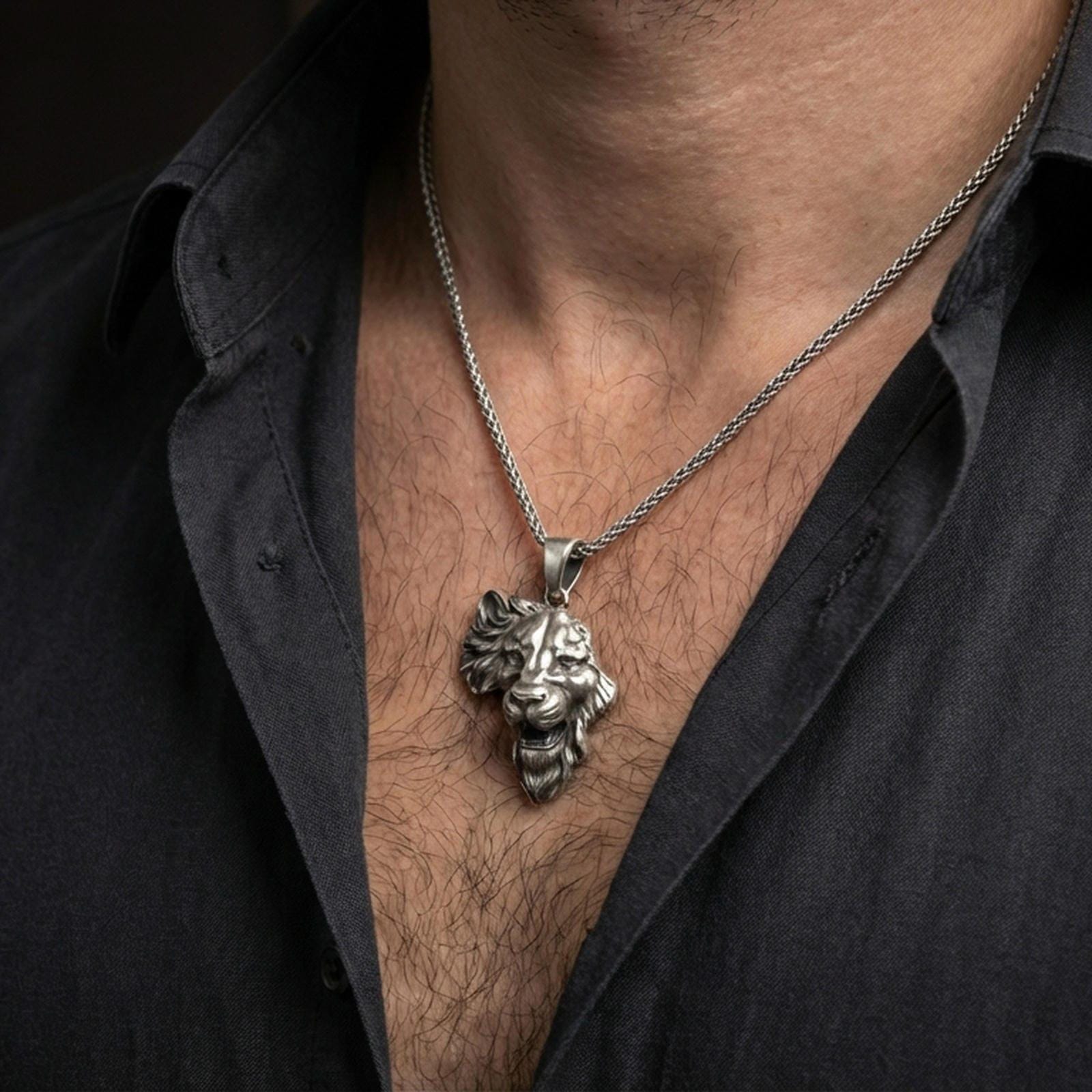 Oxidized lion head pendant necklace worn on the neck, styled in a dark lifestyle portrait with an open shirt and masculine presentation.