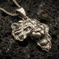 Load image into Gallery viewer, Bronze lion head pendant necklace with an oxidized finish resting on textured volcanic rock, captured in a close-up premium studio composition.
