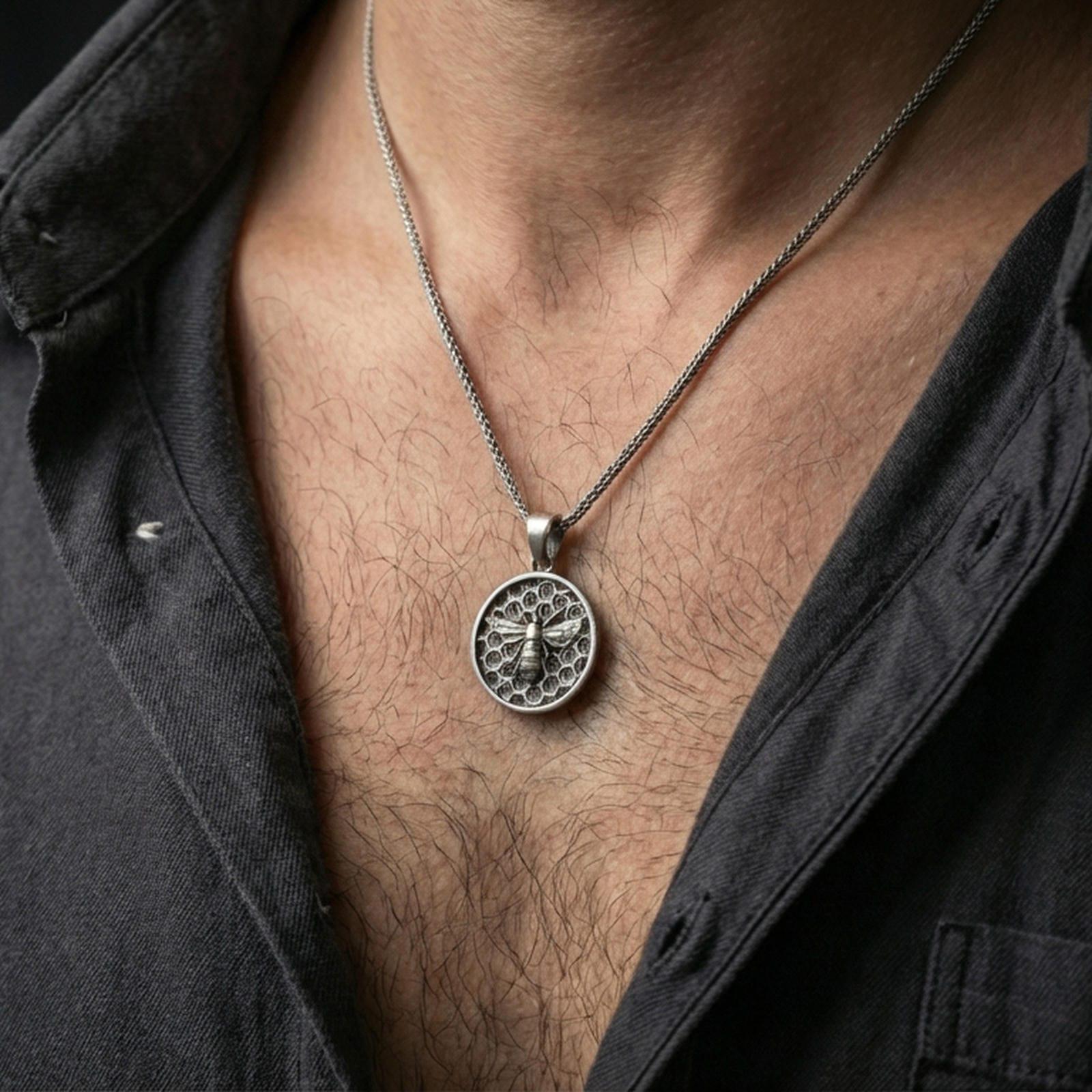 Oxidized bee pendant necklace worn on the neck, styled in a dark lifestyle portrait with an open shirt and masculine presentation.
