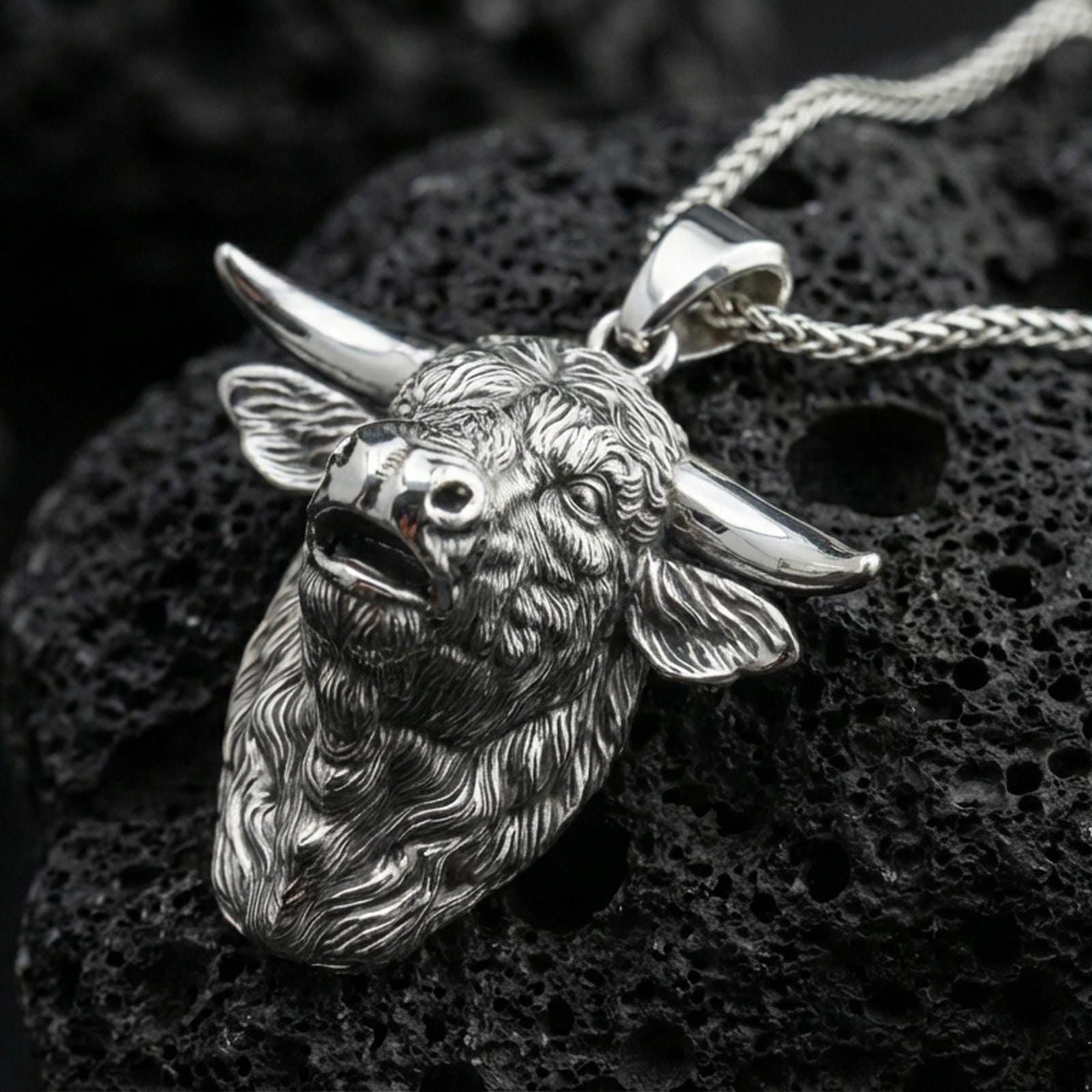 Polished silver buffalo head pendant necklace displayed on black volcanic rock, shown in a refined macro product shot with detailed horn and fur sculpting.